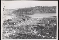 Log structures on a deforested piece of land next to a river.